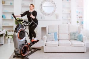 Overweight woman tries to lose pounds with time on the elliptical in her living room.
